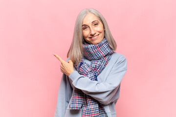 Wall Mural - middle age woman smiling cheerfully, feeling happy and pointing to the side and upwards, showing object in copy space