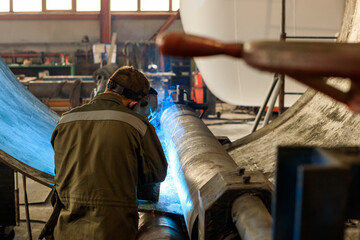 the machine in the shop near a large metal part is a welder and is doing the welding