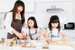 © joejoestock - Family adult parent mom teaching two small child daughter doing bakery