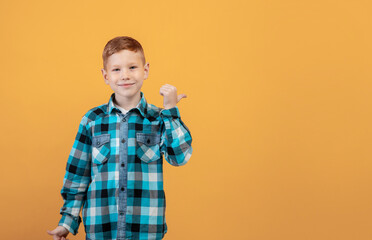 Smiling red-haired boy aiming at free space behind his back