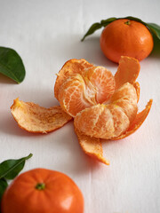 Wall Mural - Fresh juicy bright orange tangerines with green leaves on a white cotton tablecloth in the morning light