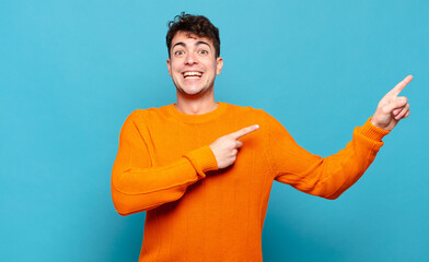 young man feeling joyful and surprised, smiling with a shocked expression and pointing to the side