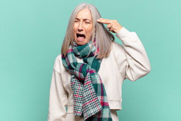 Wall Mural - middle age woman looking unhappy and stressed, suicide gesture making gun sign with hand, pointing to head