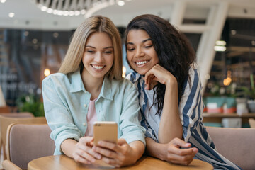 Smiling friends using mobile phone, watching video, communication in modern cafe. Happy bloggers live streaming, selective focus