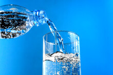Pouring Water From Plastic Bottle Into Glass On Blue Background. Stream Of Clean Water Flowing In A Glass.