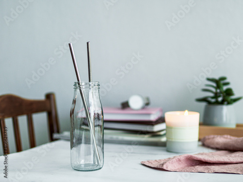 Metal drinking straws in glass bottle on white marble table indoor. Metal straws on table in living room interior. Recyclable straws, zero waste concept.