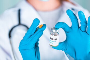 Woman doctor or nurse in uniform and gloves wearing face mask protective in lab holding medicine vial vaccine bottle with COVID-19 Coronovirus vaccine label