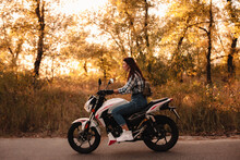 Young Confident Woman Riding Motorcycle On Country Road At Sunset