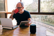 © Cavan Images - Mature man drinks from a cup while working at home