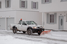 A Pickup Truck Equipped With A Plow Is Removing Snow From A Sloped Driveway In Winter. White Pickup Truck With Plow. Clearing The Streets From Snow.