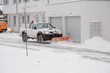 A pickup truck equipped with a plow is removing snow from a sloped driveway in winter. White pickup truck with plow. Clearing the streets from snow.