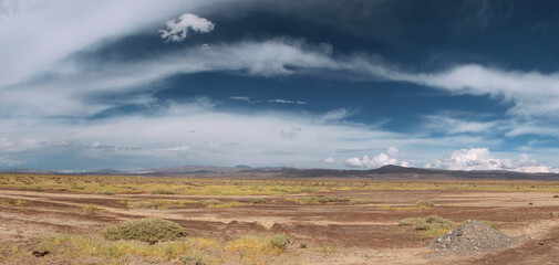 Inspirational background for quotes. Panorama view of the arid desert, valley, grass and mountains in the background under a beautiful blue sky with dramatic clouds. 