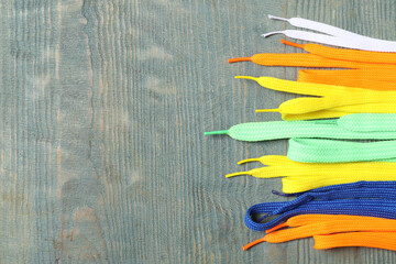 Colorful shoelaces on light blue wooden background, flat lay. Space for text