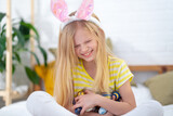 Fototapeta  - Happy Easter kids. Girl in rabbit bunny ears on head with colored eggs at home. Cheerful crazy smiling child