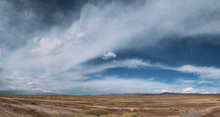 Panorama view of the arid desert, valley, grass and mountains in the background under a beautiful blue sky with dramatic clouds.