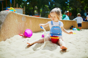 Adorable little girl having fun on playground in sandpit