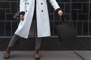 Woman holds in hand black shopping bag against black textured tile wall. Blank space, minimal brand package mock up concept, fashion blogger, space for text