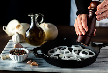 Chef grinding pepper onto white onion slices in a cast iron fry pan.