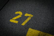 © YK - Grey asphalt road, yellow painted number twenty seven on grey street, yellow lines like a corner on the road, space for text
