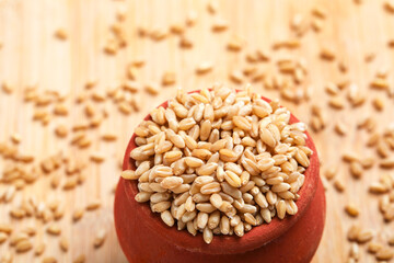 Wheat grains in clay pot on white background