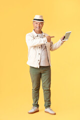 Wall Mural - Senior man pointing at tablet computer on color background
