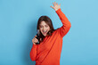 © sementsova321 - Happy crazy brunette girl in casual jumper, holding bottle with soda in hands and dancing happily isolated over blue background, keeping hands raised, yelling something, celebrating good event.,