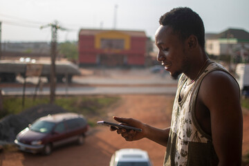 young african man using his phone late in the evening, side view