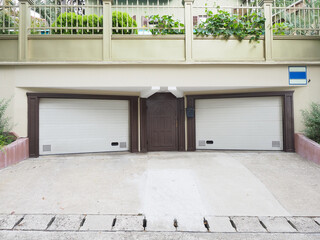 Two symmetrical garages with closed white roller shutters and an iron brown door between them