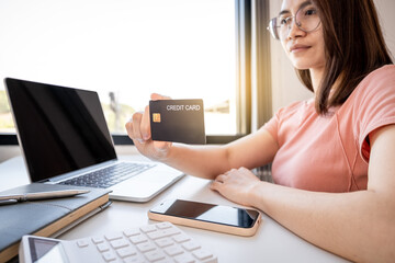 Young Asian consumer woman hand holding a credit card, Ready to spending pay online shopping according to discount products via smartphone and laptop from home