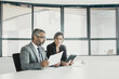 © Mangostar - Company executives analyzing and discussing reports. Two business colleagues sitting together, looking at document, holding tablet and talking. Wide shot. Communication concept