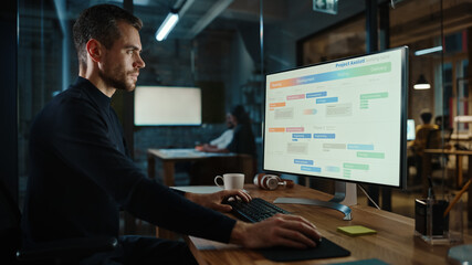 Wall Mural - Young Handsome Project Manager Working on a Marketing Presentation on Desktop Computer in Busy Creative Office. Male Specialist is Implemeting Business Strategy Points Into the Keynote.