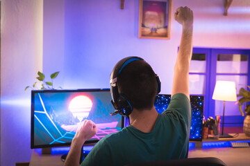 Professional gamer playing video game on his personal computer and celebrating victory. Room lit by Neon Lights in Retro Arcade Style. Cyber Championship. Footage fade out into bokeh.