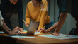 © Gorodenkoff - Close Up of Diverse Multiethnic Team Having Conversation in Meeting Room in a Creative Office. Colleagues Lean On a Conference Table, Look at Laptop Computer and Make Notes with Pencils on Notebooks.