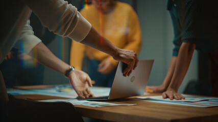 Close Up of Diverse Multiethnic Team Having Conversation in Meeting Room in a Creative Office. Colleagues Lean On a Conference Table, Look at Laptop Computer and Make Notes with Pencils on Notebooks.