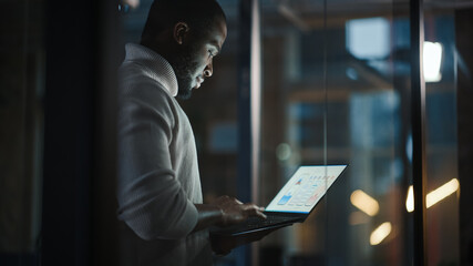 Aufkleber - Handsome Black African American Male is Standing in Meeting Room Behind Glass Walls with Laptop Computer in an Creative Agency. Project Manager Wearing White Jumper and Working on App User Interface.