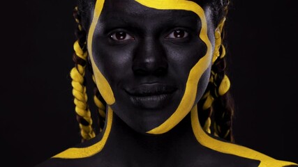 Wall Mural - Face art. Woman with black and yellow body paint. Young african girl with colorful bodypaint. An amazing afro american model with yellow makeup. Closeup face.