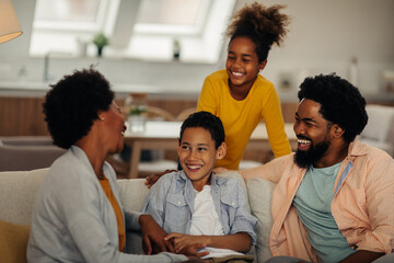 Wall Mural - Afro parents and their children are socializing while sitting on the sofa in the living room