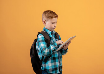 Ginger kid schooler using digital tablet on yellow