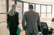 © Mangostar - Male CEO and female assistant wearing suits, walking in meeting room. Woman holding folder. Back view. Business communication concept