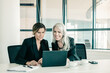 © Mangostar - Cheerful business ladies looking at laptop display, talking and smiling while sitting at table with cups of coffee in office. Teamwork and communication concept