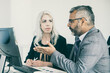 © Mangostar - Two serious managers watching presentation on pc monitor, discussing project, sitting at desk with paper diagram. Business communication concept