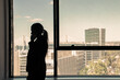 © Mangostar - Unrecognizable silhouette of businesswoman standing near window and talking on mobile phone. Professional manager in shadow and cityscape on background. Business, communication and company concept