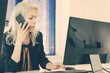 © Mangostar - Businesswoman sitting in office and talking on phone. Grey-haired confident employee typing on computer keyboard and discussing work with client via smartphone. Business and communication concept