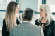 © Mangostar - Female managers talking to male boss, standing in office, discussing project. Medium shot, back view. Business communication or briefing concept