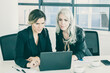 © Mangostar - Serious female professionals looking at laptop display while sitting at table with cups of coffee and papers in office. Front view. Teamwork and communication concept