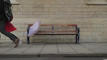 Wide Shot Of Discarded Umbrella On Bench As People Walk Past