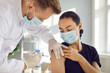 Young man in medical face mask getting flu shot during seasonal infection outbreak. Male doctor or nurse giving effective Covid-19 vaccine injection to patient during modern vaccination campaign