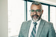 © Mangostar - Content Indian CEO standing and smiling for portrait. Successful pensive bearded businessman in glasses posing in office room and looking at camera. Business, expression and management concept