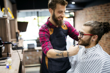 Happy young handsome man visiting hairstylist in barber shop salon