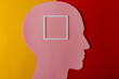 Head silhouette made of paper and plastic frame. Pink paper shaped as a human head with copy space on yellow and dark red paper background.